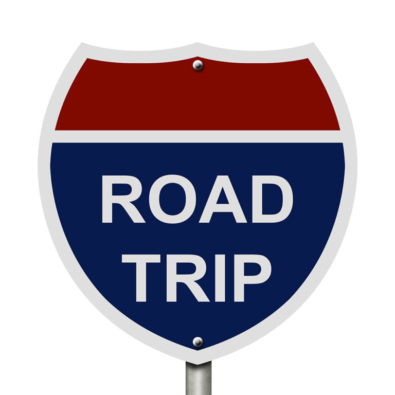 A road sign in red, white, and blue reads ROAD TRIP in bold white letters.